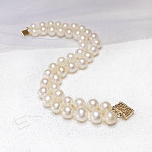 May include: A double strand pearl bracelet with a gold clasp. The pearls are white and round.