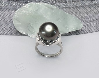 Könnte beinhalten: Ein silberner Ring mit einem großen, dunkelgrauen Perlmutt, das in einem strukturierten, wellenförmigen Design gefasst ist.