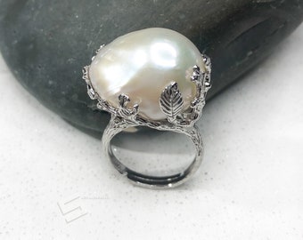 May include: A silver ring with a large white baroque pearl set in a delicate branch design.