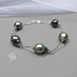 Può includere: Un braccialetto a catena d'argento con cinque perle grigio scuro. Le perle sono grandi e hanno un bagliore iridescente.