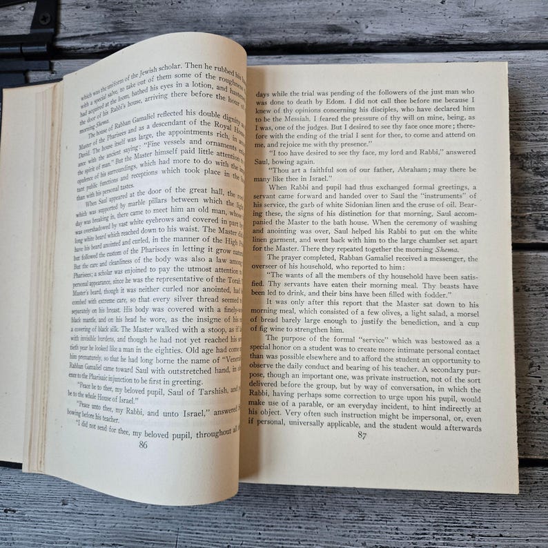 May include: Open book with text on aged paper. The pages are yellowed, and the text is in black. The book is open to a double-page spread, with text filling both pages. The book is on a dark surface.