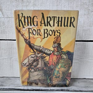 May include: Vintage book cover titled "King Arthur For Boys." The illustration depicts a knight in shining armor on horseback, holding a spear with a banner. The background is a yellow and orange gradient.