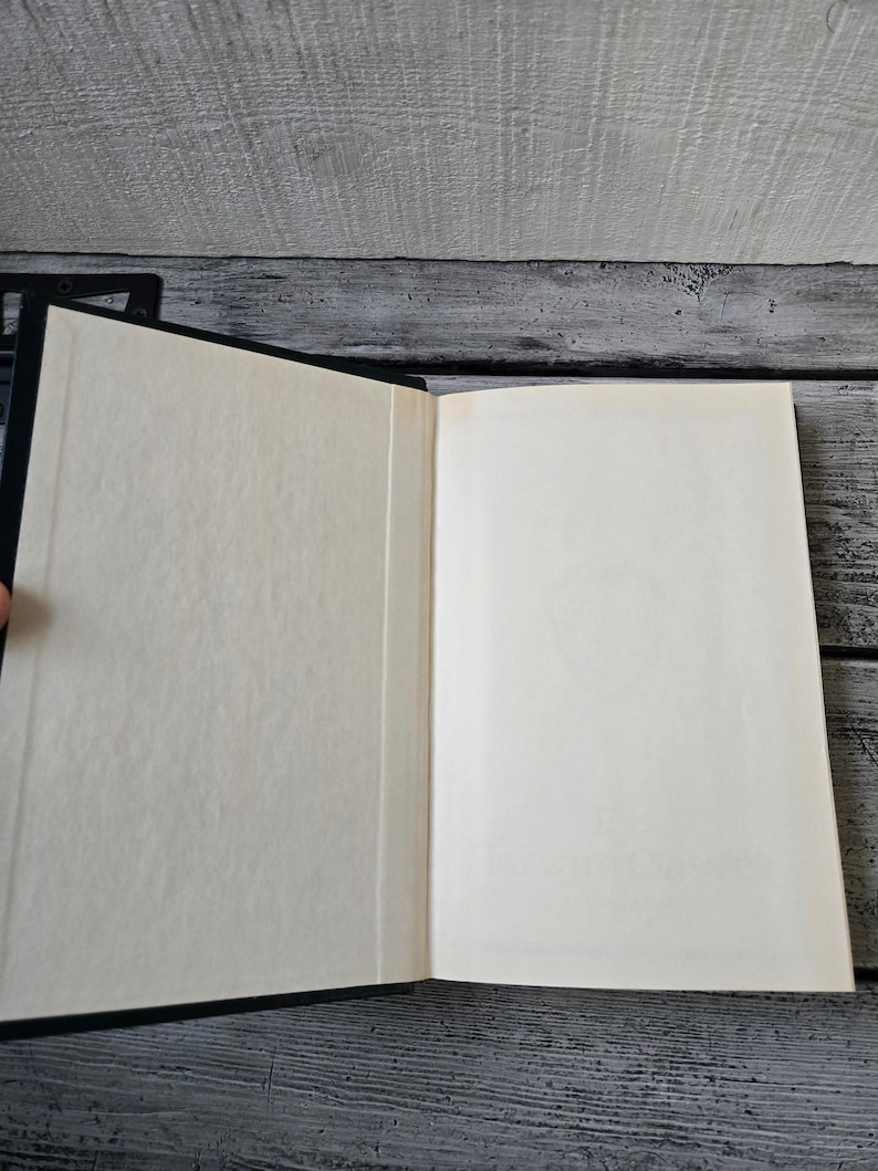 May include: A black hardback book with a blank white interior. The book is open and lying flat on a wooden surface.
