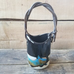May include: A small black ceramic vase with a white and blue glaze, featuring a twisted wire handle.