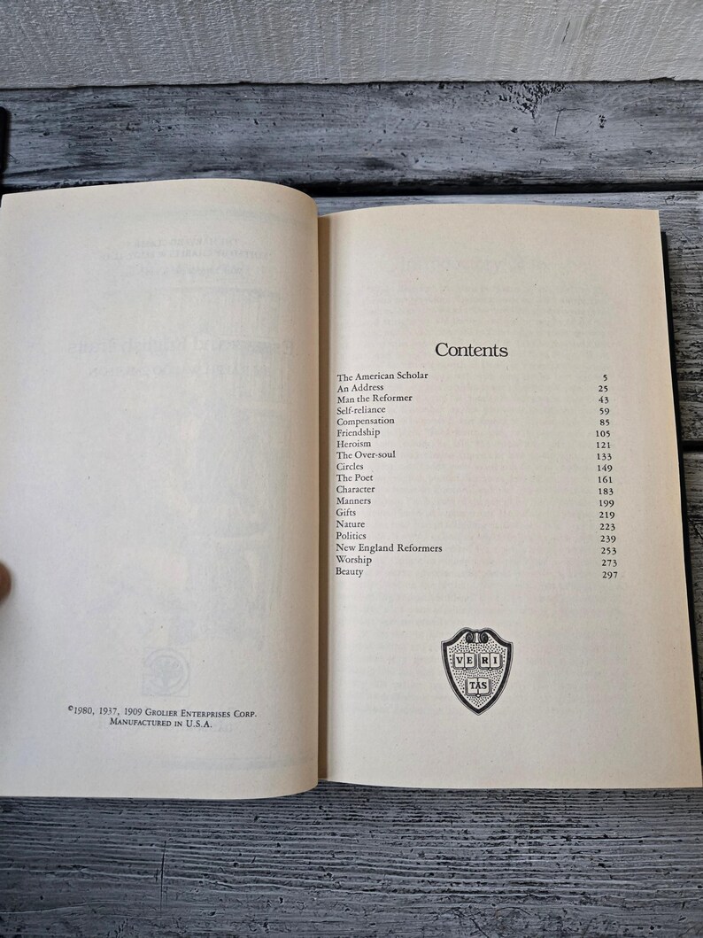May include: A book titled "The American Scholar" by Ralph Waldo Emerson. The book contains a table of contents with essays such as "Self-reliance", "Compensation", "Friendship", and "Heroism".