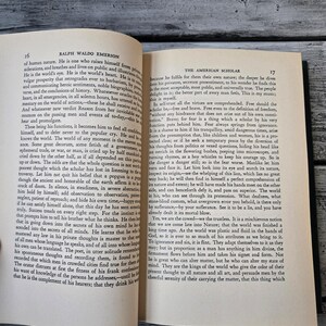 May include: An open book with a tan cover and black text. The book is titled "The American Scholar" by Ralph Waldo Emerson. The text on the page discusses the importance of self-trust and bravery for a scholar.