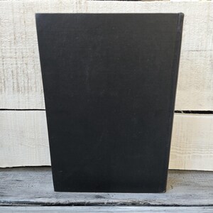 May include: A solid black, rectangular object with a slightly trapezoidal shape. The object is positioned upright against a white and gray wooden surface. The object's surface appears smooth and matte.