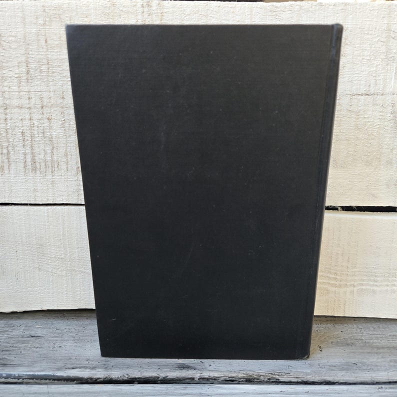 May include: A solid black, rectangular object with a slightly trapezoidal shape. The object is positioned upright against a white and gray wooden surface. The object's surface appears smooth and matte.