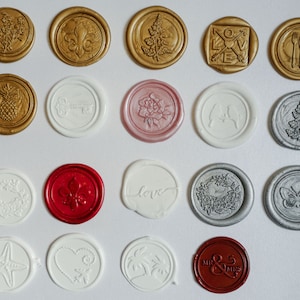 May include: Assortment of 18 wax seals with various designs, including floral, geometric, and abstract patterns. The seals are in gold, silver, red, white, and pink.