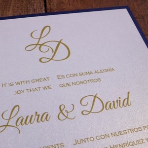 May include: A white wedding invitation with a navy blue border. The invitation features gold lettering with the names Laura & David and the text "It is with great joy that we... Es con suma alegr&iacute;a que nosotros... Junto con nuestros padres... Henr&iacute;quez y..."