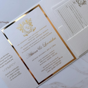 May include: Elegant wedding invitation with gold foil accents. The invitation features the names Athina and Leonidas, along with the wedding date and location. Includes a separate RSVP card. The design is classic and sophisticated.