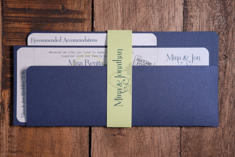 May include: Navy blue wedding invitation suite with a light green belly band. The invitation includes text that reads "Mira & Jonathan" and "Mira & Jon Wedding 2016". The suite is on a wooden surface.