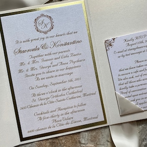 May include: A white and gold wedding invitation with a gold ribbon. The invitation features the couple's names, "Stavroula & Konstantino", the date of the wedding, "September 5th, 2021", and the location of the ceremony and reception. The invitation also includes a RSVP card with the couple's contact information.