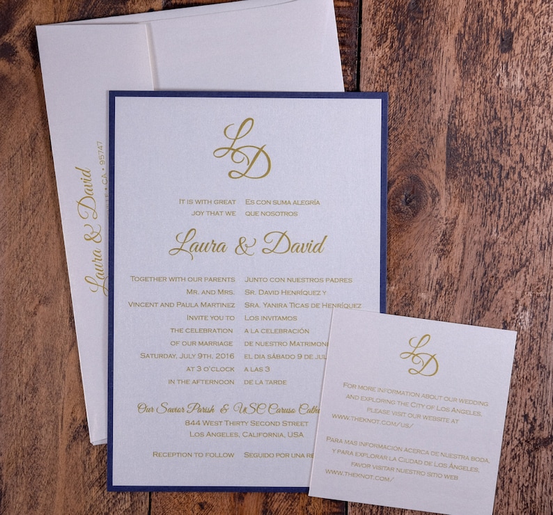 May include: A wedding invitation with a navy blue border and gold lettering. The invitation is for Laura and David and includes the date, time, and location of the wedding. The invitation also includes the text "It is with great joy that we..." and "Es con suma alegr&iacute;a que nosotros..."