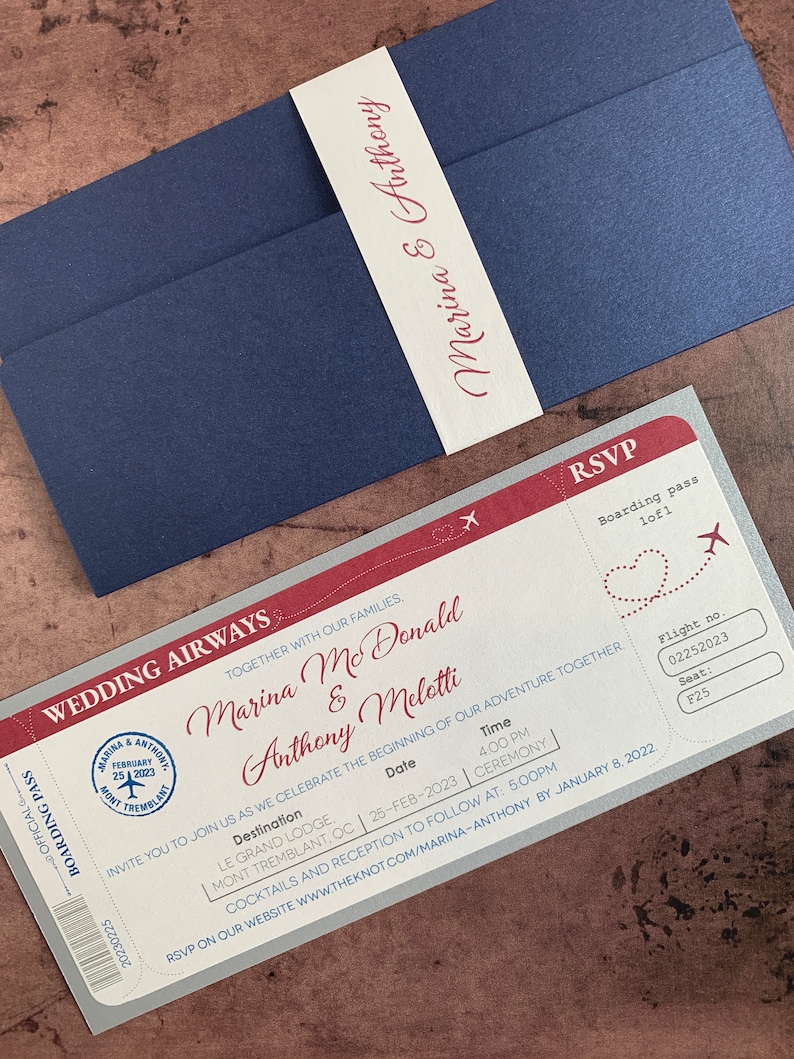 May include: A navy blue wedding invitation suite featuring a boarding pass design. The invitation includes the names "Marina & Anthony", date, time, and location details. A matching belly band with the names "Marina & Anthony" wraps the invitation.
