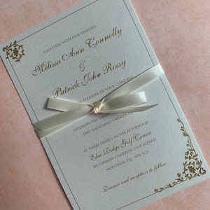 May include: Elegant wedding invitation with gold script and floral accents. The invitation is tied with a cream-colored ribbon. The text includes the names Melissa Ann Connolly and Patrick John Rossy, along with the wedding details.