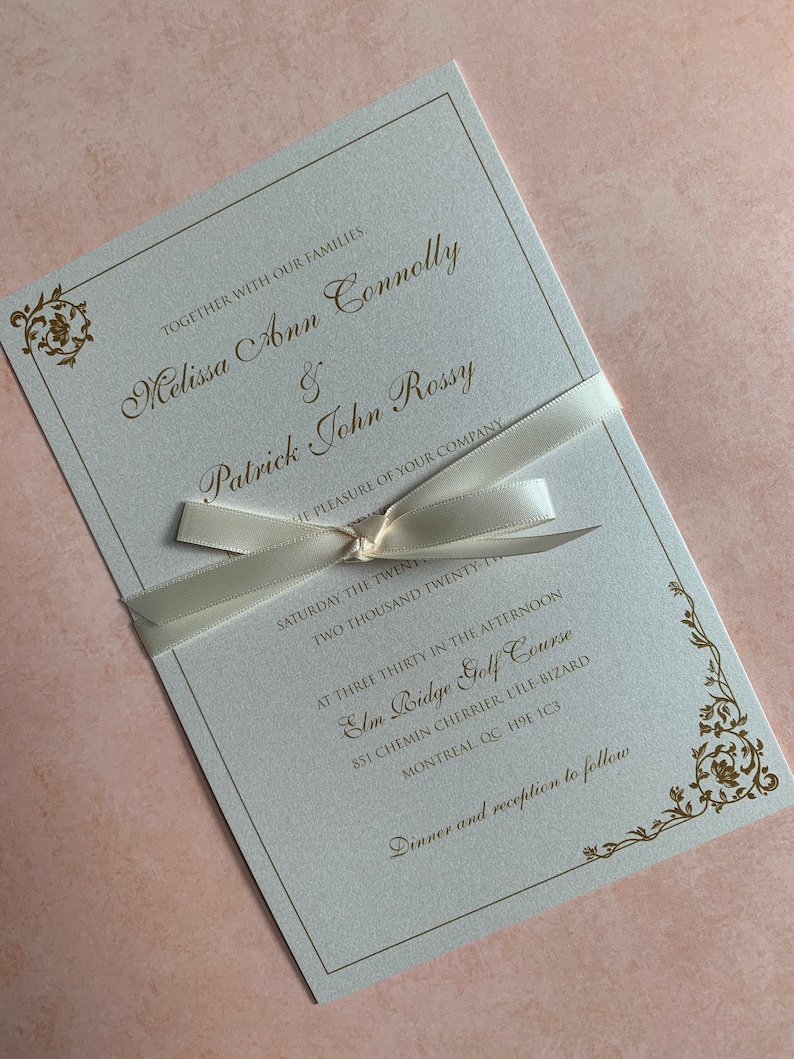 May include: Elegant wedding invitation with gold script and floral accents. The invitation is tied with a cream-colored ribbon. The text includes the names Melissa Ann Connolly and Patrick John Rossy, along with the wedding details.