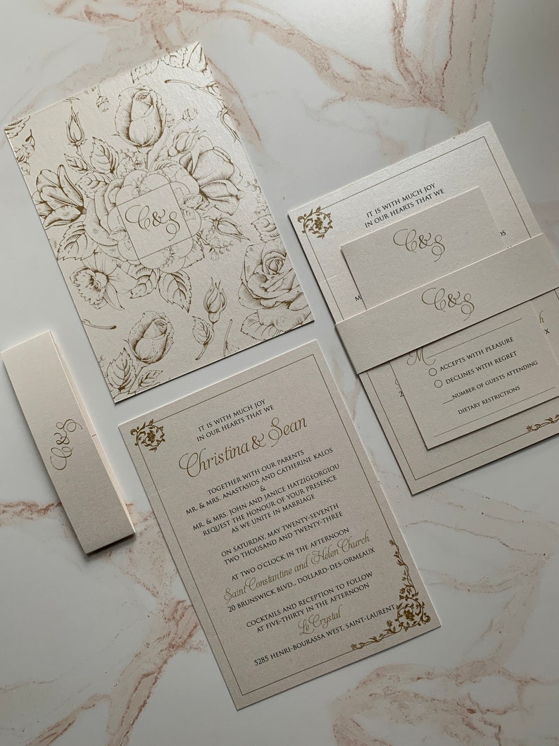May include: Elegant wedding invitation suite in cream with gold floral accents. The suite includes a main invitation, RSVP card, enclosure card, and a belly band, all featuring the initials "C&S". The main invitation includes the names Christina & Sean.