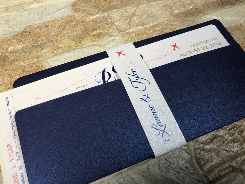 May include: Navy blue wedding invitation suite with a white belly band. The invitation features the names "Leanne & Tyler" in elegant script. The band is decorated with red airplane graphics and the text "Kindly reply by August 22, 2018."