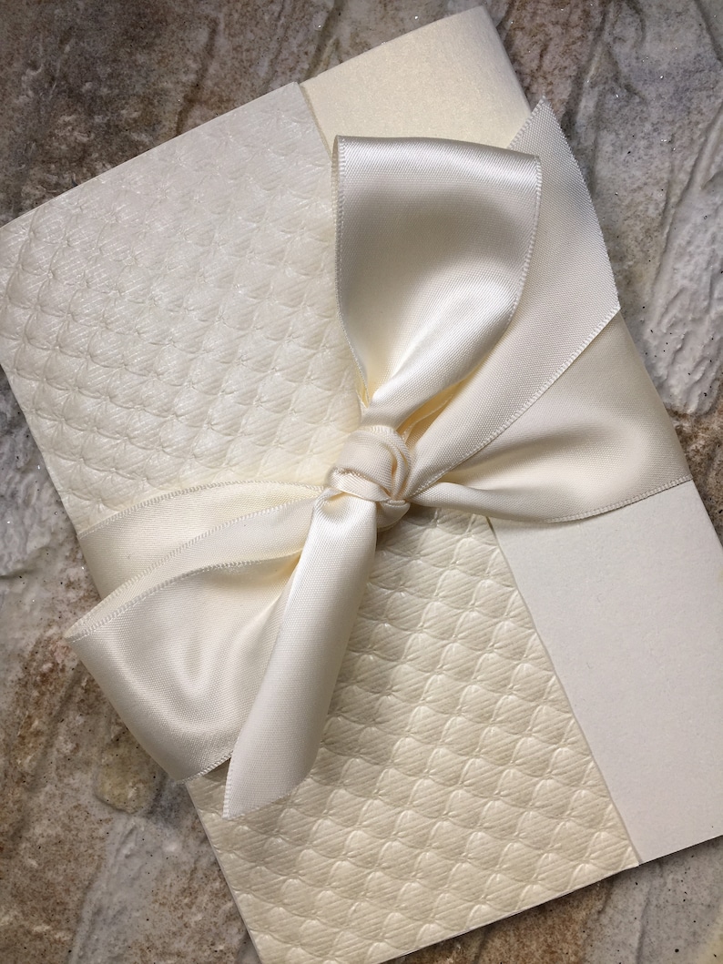 May include: A white invitation card with a white satin ribbon tied in a bow. The card has a textured pattern.