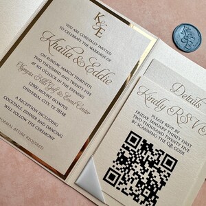 May include: Gold and white wedding invitation with a gold border and a white ribbon. The invitation includes the names Khaila & Eddie, the date and time of the wedding, and the location. The invitation also includes a QR code for RSVP.