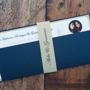 May include: A navy blue wedding invitation suite with a light green backing. The invitation features the names "Aida & Genevieve" on a light green band. The invitation includes a photo of two people.