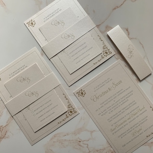 May include: Elegant ivory wedding invitation suite with gold foil accents. Includes invitation, RSVP card, belly band, and details card. Features floral corner designs and the initials "C&S".