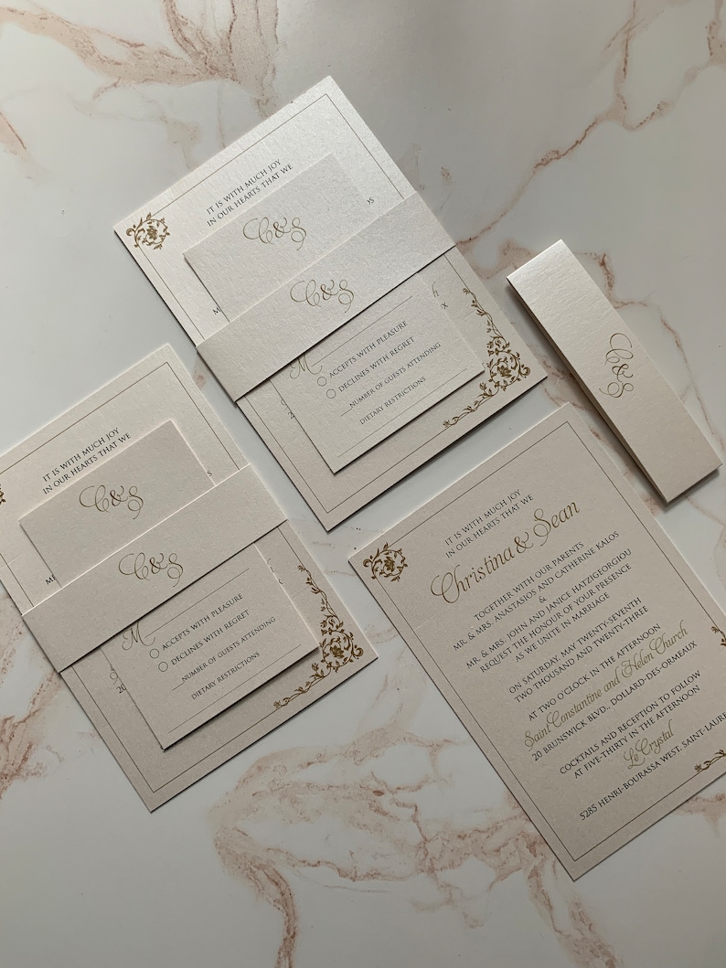 May include: Elegant ivory wedding invitation suite with gold foil accents. Includes invitation, RSVP card, belly band, and details card. Features floral corner designs and the initials "C&S".