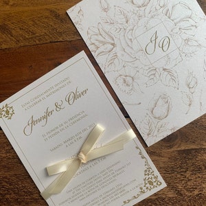 May include: Elegant wedding invitation set featuring a cream-colored card with gold floral accents and the names "Jennifer & Oliver." The invitation is tied with a cream ribbon. A matching card with floral design is also included.