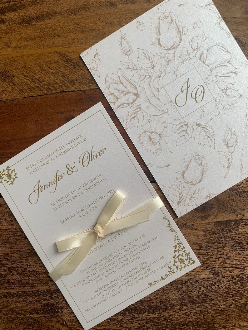 May include: Elegant wedding invitation set featuring a cream-colored card with gold floral accents and the names "Jennifer & Oliver." The invitation is tied with a cream ribbon. A matching card with floral design is also included.