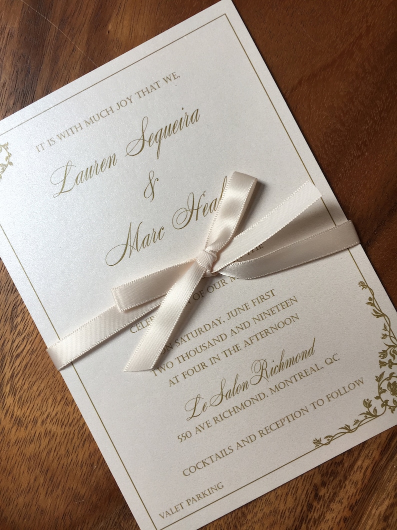 May include: Ivory wedding invitation with gold lettering and a cream-colored ribbon. The invitation includes the names Lauren Sequeira & Marc Heal, event details, and venue information.