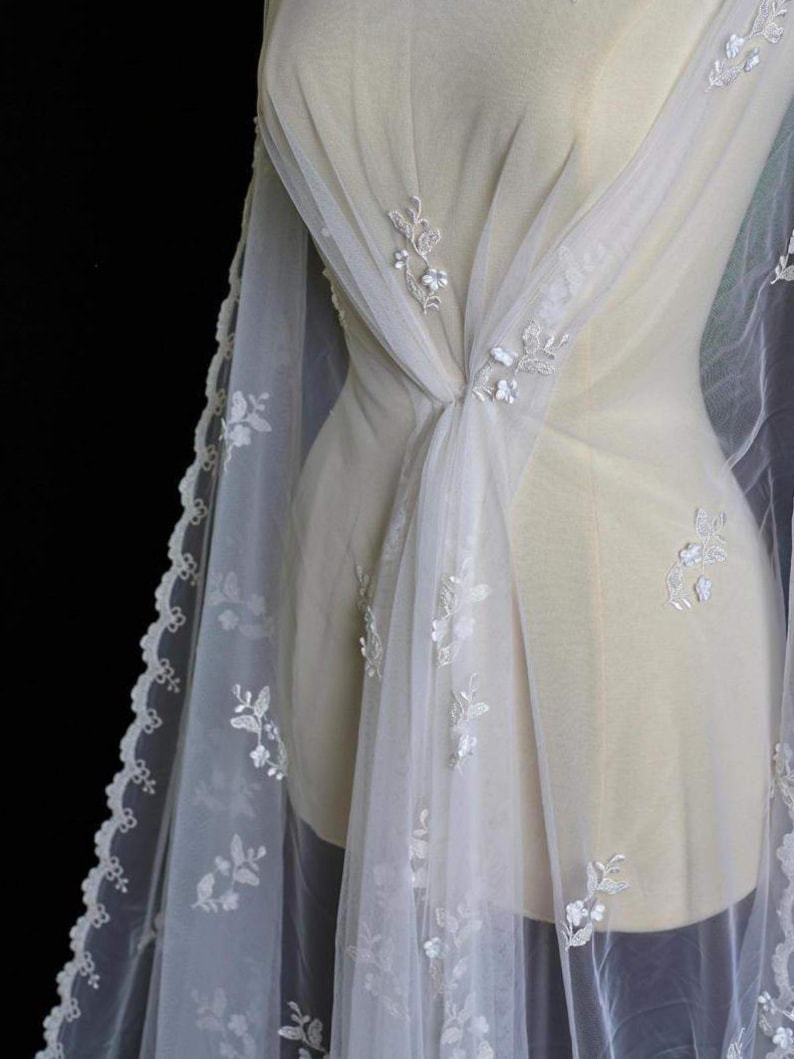 Puede incluir: Tela de tul blanco con delicado bordado floral. La tela tiene un borde festoneado y es transparente y ligera.