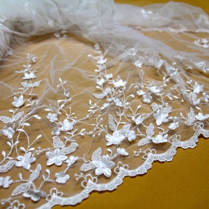 Puede incluir: Tela de encaje blanca con un delicado patr&oacute;n floral. El encaje tiene un borde festoneado y est&aacute; hecho de un material ligero y transparente.