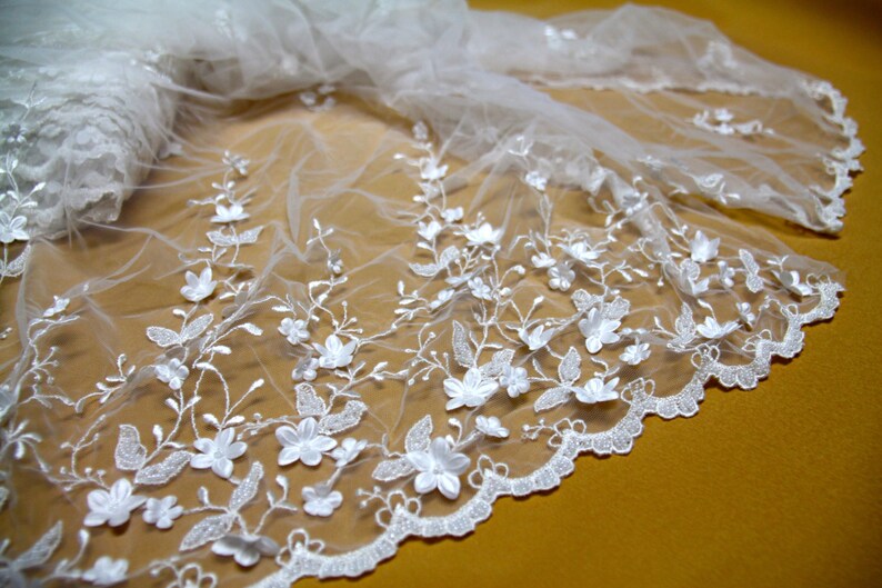 Puede incluir: Tela de encaje blanca con un delicado patr&oacute;n floral. El encaje tiene un borde festoneado y est&aacute; hecho de un material ligero y transparente.