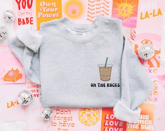 May include: A gray sweatshirt with a graphic of a coffee drink with ice cubes and the text "ON THE ROCKS" printed on the front.
