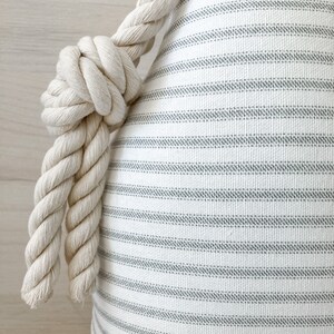 May include: A white and gray striped pillow with a thick, white rope tied around the top.