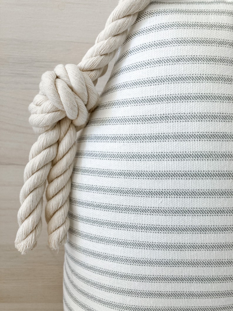 May include: A white and gray striped pillow with a thick, white rope tied around the top.