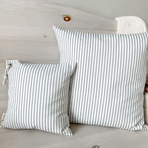 May include: Two striped throw pillows, one larger than the other, with a white background and thin blue stripes. The pillows are sitting on a white wooden bench.
