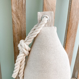 May include: A beige doorstop with a rope handle and blue stripes. The doorstop has a metal ring on the top.