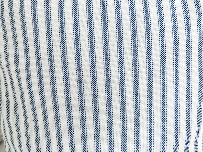 May include: White fabric with thin blue stripes. The fabric has a subtle texture.