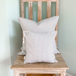 May include: Two striped throw pillows in white and gray are placed on a weathered wooden chair. The pillows are made of a soft, woven fabric and have a simple, classic design.
