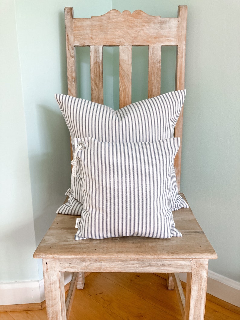 May include: Two striped throw pillows in white and gray are placed on a weathered wooden chair. The pillows are made of a soft, woven fabric and have a simple, classic design.
