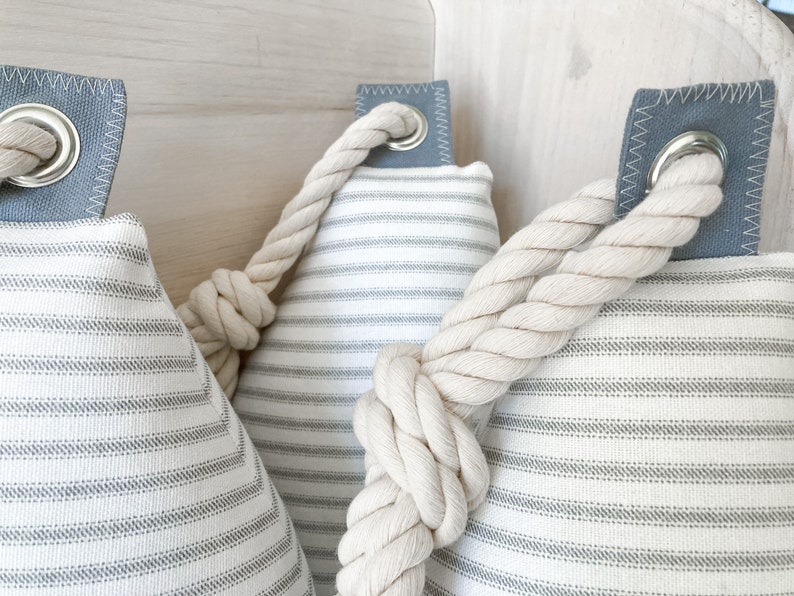 May include: Three white and gray striped fabric doorstops with a thick white rope tied around them. The doorstops have a gray fabric loop with a metal ring.