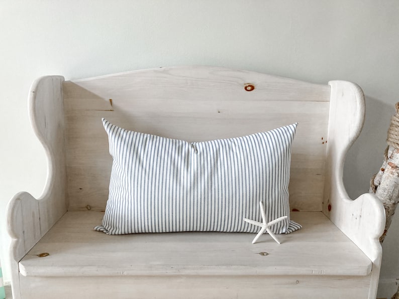 May include: A white wooden bench with a blue and white striped pillow and a white starfish on the seat.