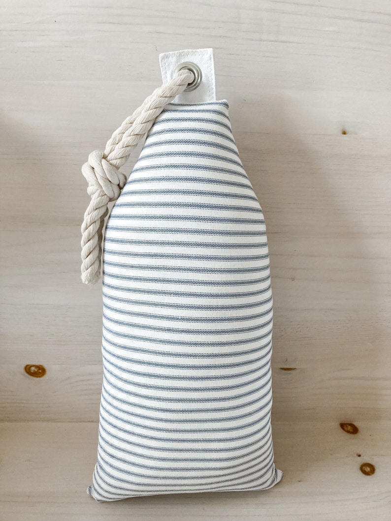 May include: A white and blue striped fabric doorstop with a rope handle and a metal eyelet.