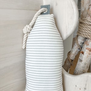May include: A white and gray striped pillow with a rope loop and a gray fabric tab. The pillow is hanging on a white wooden surface.