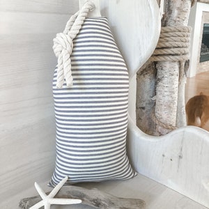 May include: A white and blue striped pillow with a rope handle. The pillow is sitting on a white bench with a piece of driftwood and a white starfish.