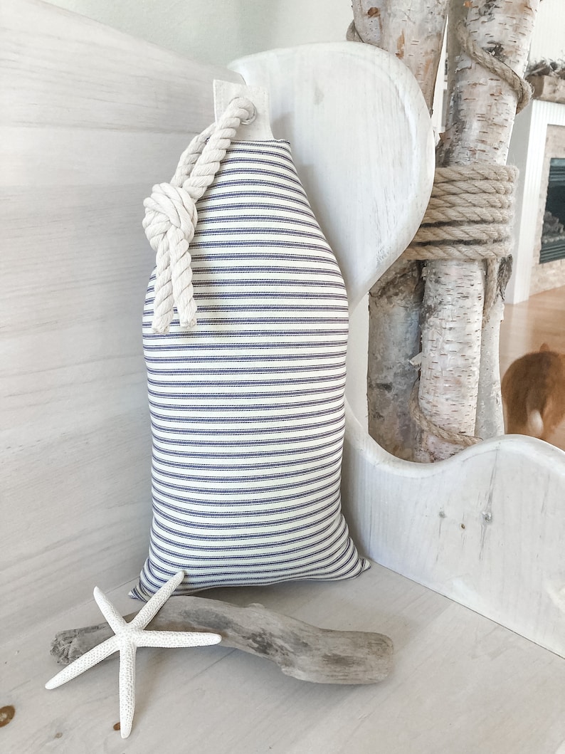 May include: A white and blue striped pillow with a rope handle. The pillow is sitting on a white bench with a piece of driftwood and a white starfish.