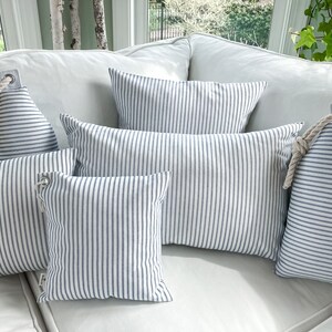 May include: Five blue and white striped throw pillows with rope accents on a white couch.