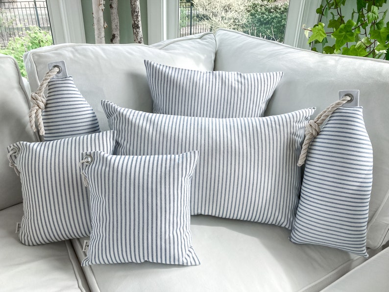 May include: Five blue and white striped throw pillows with rope accents on a white couch.